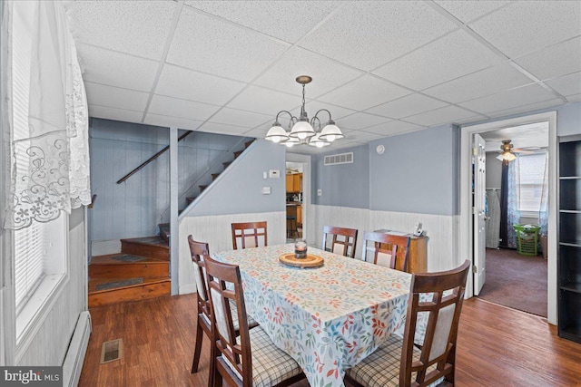 dining space featuring ceiling fan with notable chandelier, baseboard heating, a drop ceiling, and dark wood-type flooring