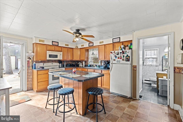 kitchen with ceiling fan, a center island, a kitchen breakfast bar, baseboard heating, and white appliances