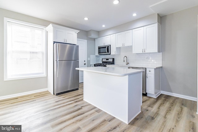 kitchen with a kitchen island, appliances with stainless steel finishes, tasteful backsplash, light hardwood / wood-style floors, and white cabinetry