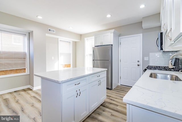 kitchen with light stone countertops, sink, a center island, white cabinets, and appliances with stainless steel finishes