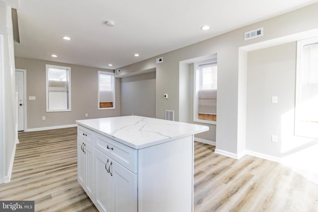 kitchen with light stone countertops, light hardwood / wood-style flooring, white cabinetry, and a kitchen island