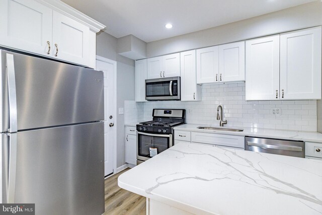 kitchen with white cabinetry, sink, stainless steel appliances, backsplash, and light hardwood / wood-style floors