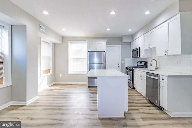 kitchen with a center island, white cabinetry, appliances with stainless steel finishes, and light hardwood / wood-style flooring