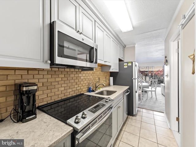 kitchen with light tile patterned floors, ornamental molding, appliances with stainless steel finishes, tasteful backsplash, and white cabinetry