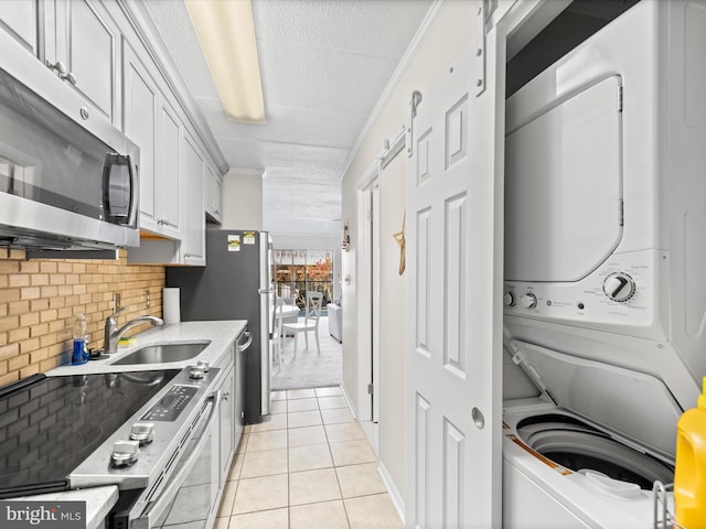 kitchen featuring appliances with stainless steel finishes, crown molding, light tile patterned floors, white cabinets, and stacked washer / drying machine