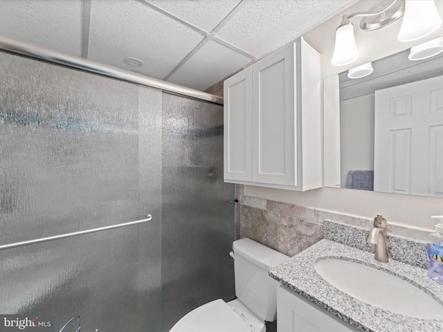 bathroom featuring vanity, a paneled ceiling, toilet, and a shower with shower door