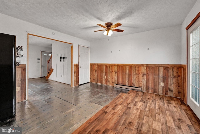 spare room with a textured ceiling, wooden walls, ceiling fan, and a baseboard heating unit