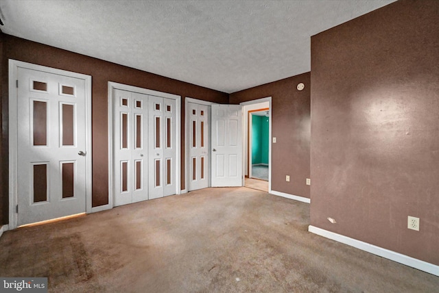 unfurnished bedroom with a textured ceiling, carpet floors, and multiple closets