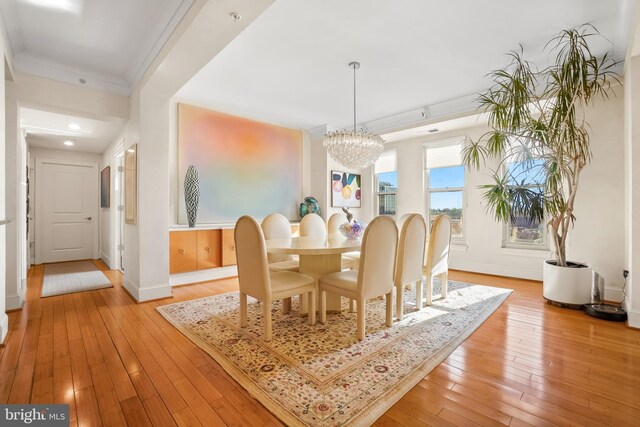 dining space with crown molding, light hardwood / wood-style flooring, and an inviting chandelier