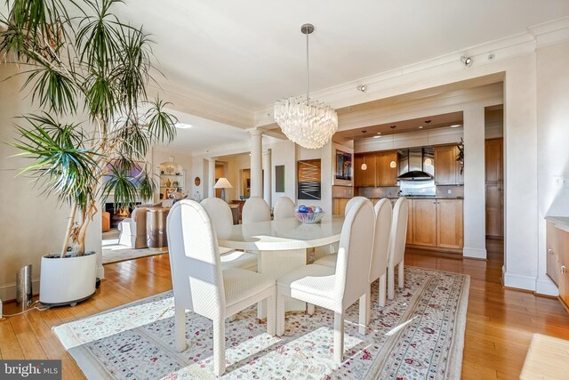 dining room featuring light hardwood / wood-style floors, ornate columns, ornamental molding, and a chandelier