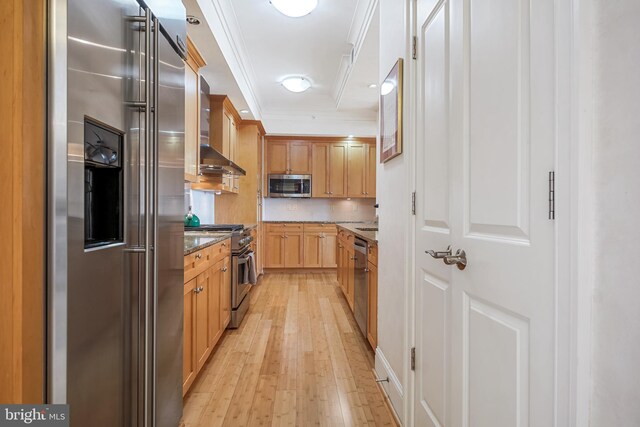 kitchen featuring light wood-type flooring, wall chimney exhaust hood, crown molding, high quality appliances, and dark stone countertops