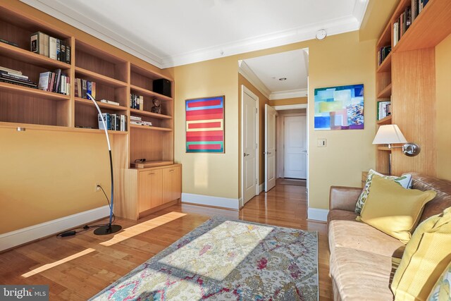 sitting room with built in shelves, hardwood / wood-style flooring, and ornamental molding