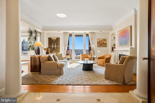 living room featuring built in shelves, wood-type flooring, crown molding, and decorative columns