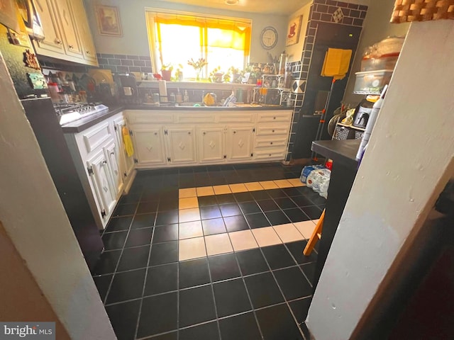 kitchen featuring white cabinets, backsplash, dark tile patterned flooring, and stainless steel gas cooktop