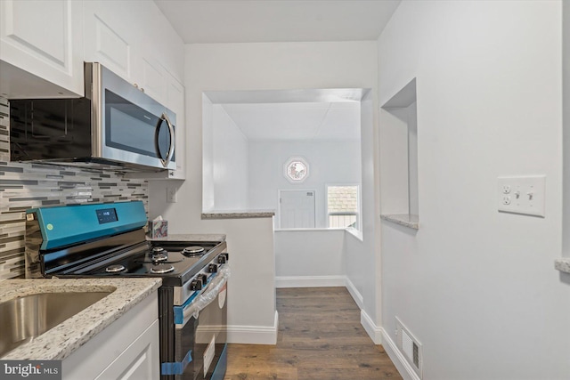 kitchen featuring light stone countertops, dark wood-type flooring, backsplash, white cabinets, and appliances with stainless steel finishes