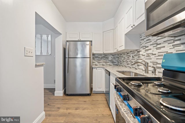 kitchen with white cabinetry, light stone countertops, backsplash, light hardwood / wood-style floors, and appliances with stainless steel finishes