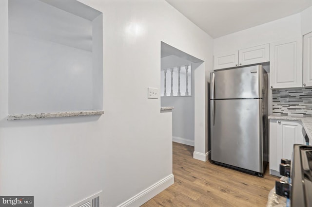 kitchen featuring stainless steel appliances, light stone counters, decorative backsplash, white cabinets, and light wood-type flooring