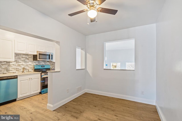 kitchen featuring white cabinets, decorative backsplash, ceiling fan, light wood-type flooring, and stainless steel appliances