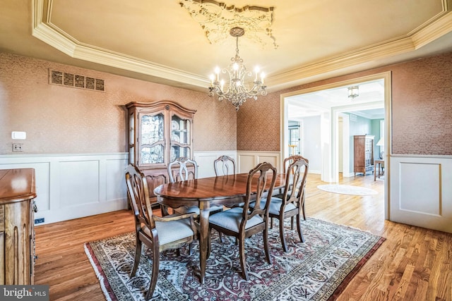 dining area with an inviting chandelier, crown molding, a tray ceiling, and light hardwood / wood-style flooring