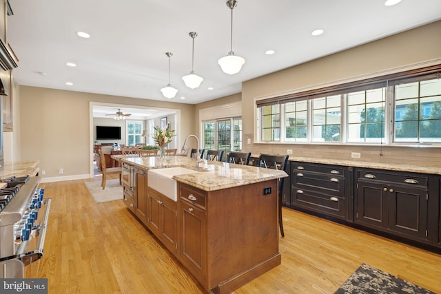 kitchen with a kitchen island with sink, hanging light fixtures, sink, light hardwood / wood-style flooring, and ceiling fan