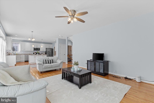 living room with recessed lighting, ceiling fan with notable chandelier, light wood-type flooring, and baseboards