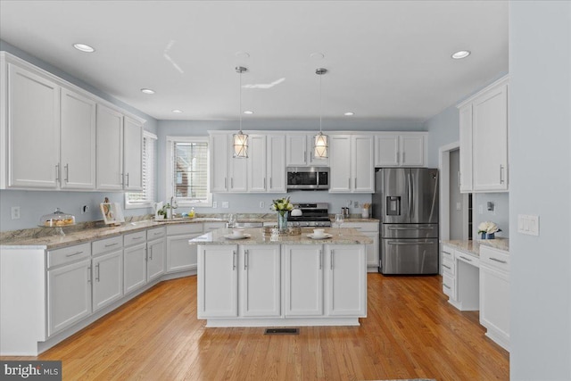 kitchen featuring decorative light fixtures, a kitchen island, appliances with stainless steel finishes, white cabinets, and light wood finished floors