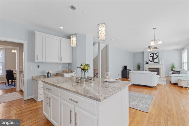 kitchen featuring a kitchen island, pendant lighting, light wood-type flooring, a fireplace, and white cabinetry