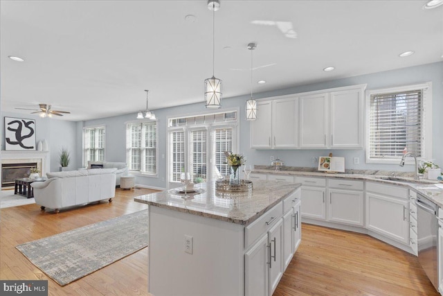 kitchen with white cabinetry, a high end fireplace, a sink, light wood-style floors, and stainless steel dishwasher