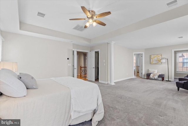 carpeted bedroom with a raised ceiling, baseboards, visible vents, and ornate columns