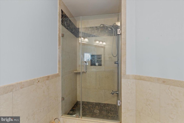 bathroom with wainscoting, a stall shower, and tile walls