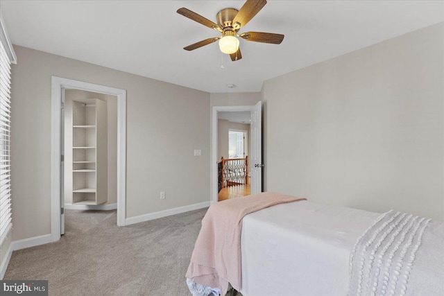 bedroom featuring a spacious closet, light colored carpet, baseboards, and ceiling fan