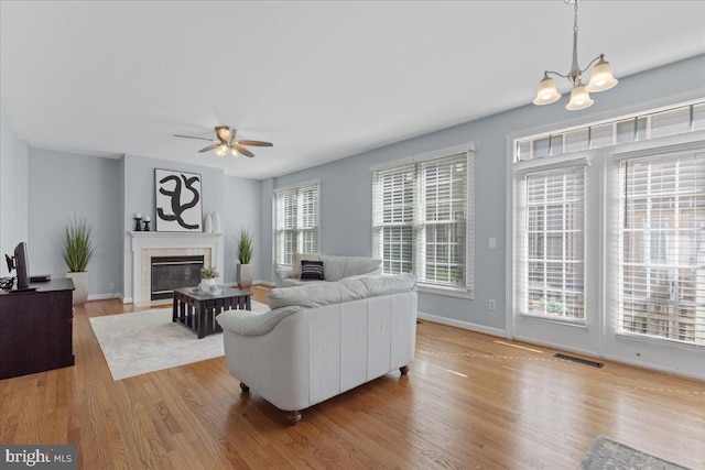 living area featuring wood finished floors, visible vents, baseboards, a fireplace with flush hearth, and ceiling fan with notable chandelier