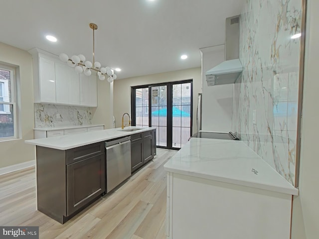 kitchen with sink, decorative light fixtures, dishwasher, white cabinets, and wall chimney range hood