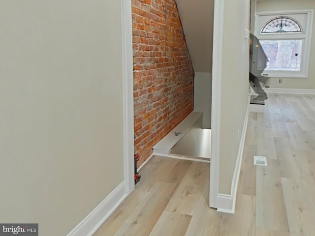 hallway with vaulted ceiling, brick wall, and light hardwood / wood-style floors