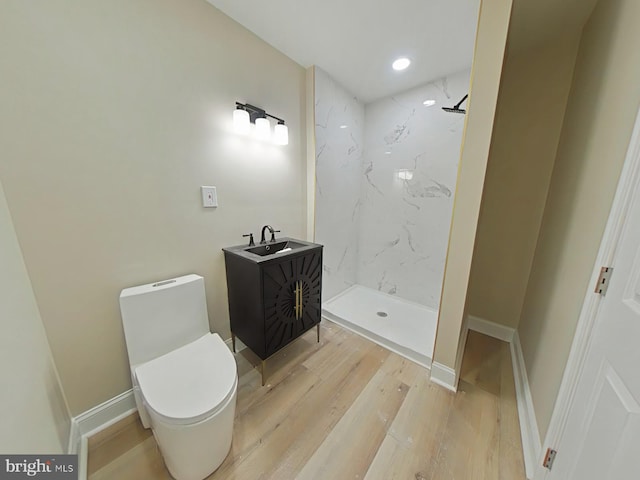 bathroom with hardwood / wood-style floors, vanity, a tile shower, and toilet