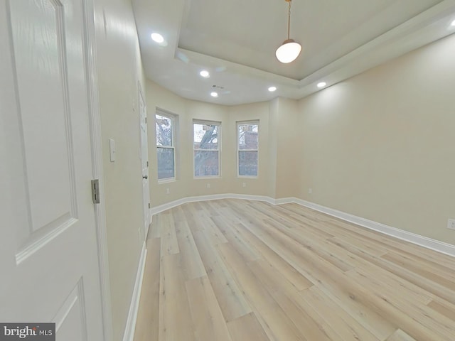 empty room featuring a tray ceiling and light hardwood / wood-style flooring