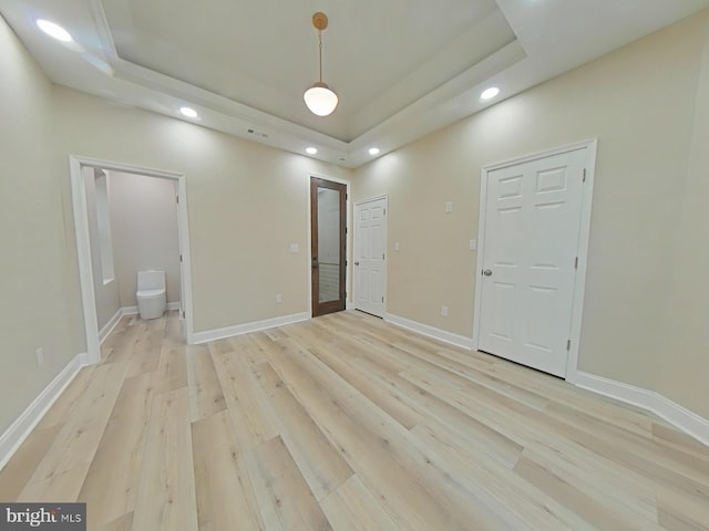 unfurnished bedroom featuring ensuite bathroom, a tray ceiling, and light hardwood / wood-style flooring