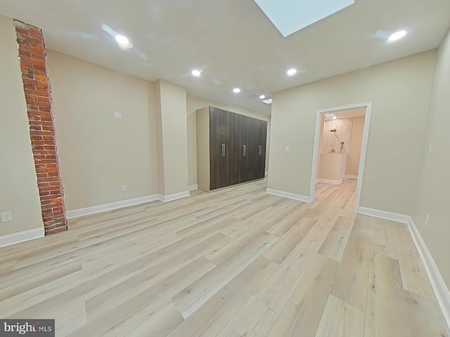 empty room with a skylight and light hardwood / wood-style flooring