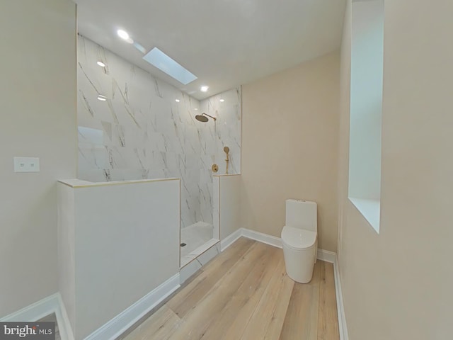 bathroom with hardwood / wood-style flooring, a skylight, a tile shower, and toilet