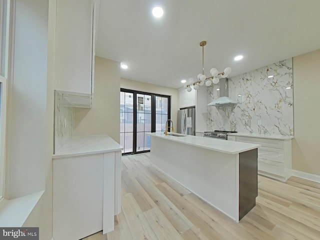 kitchen featuring white cabinetry, hanging light fixtures, stainless steel appliances, decorative backsplash, and wall chimney range hood