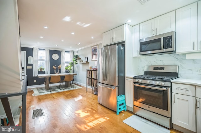 kitchen with appliances with stainless steel finishes, light hardwood / wood-style floors, white cabinetry, and ornamental molding