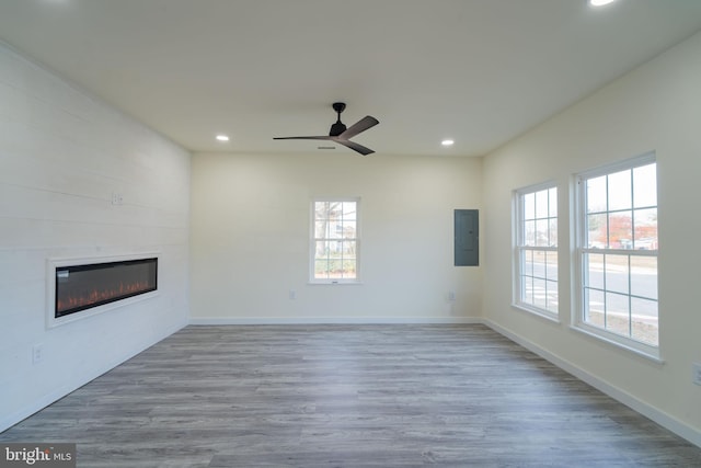 unfurnished living room featuring a large fireplace, electric panel, light hardwood / wood-style flooring, and a wealth of natural light