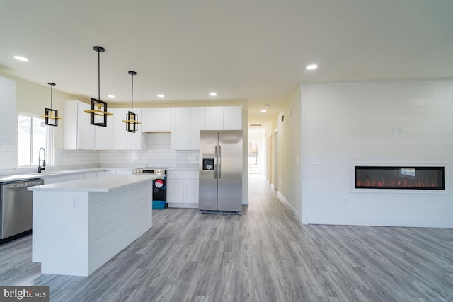 kitchen featuring appliances with stainless steel finishes, a kitchen island, decorative light fixtures, light hardwood / wood-style flooring, and white cabinetry