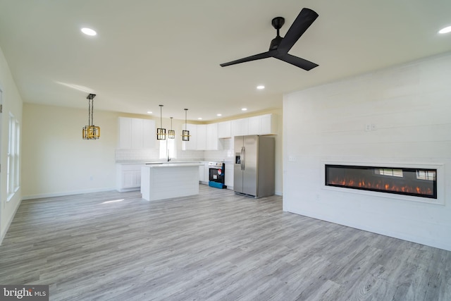 unfurnished living room featuring ceiling fan, a large fireplace, and light hardwood / wood-style flooring