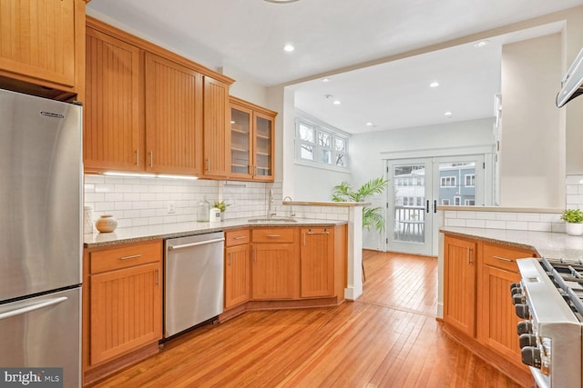 kitchen with stainless steel appliances, french doors, sink, light stone counters, and light hardwood / wood-style flooring