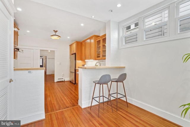 kitchen featuring light hardwood / wood-style flooring, kitchen peninsula, backsplash, a breakfast bar area, and stainless steel fridge