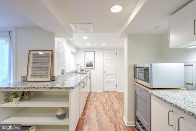 kitchen with light stone countertops, white cabinets, light hardwood / wood-style flooring, and sink