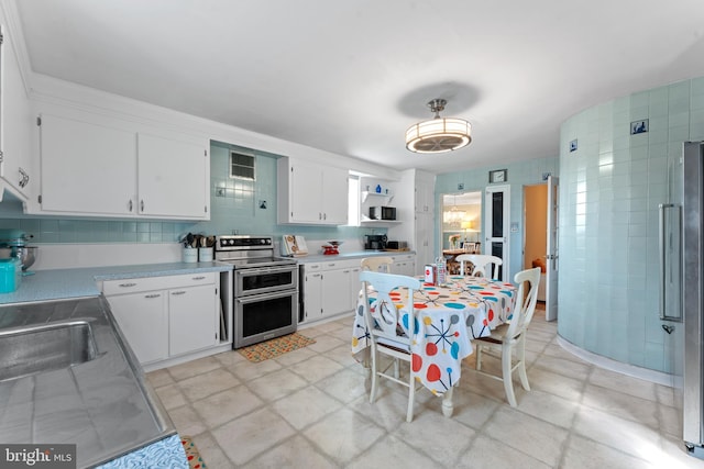 kitchen with decorative backsplash, appliances with stainless steel finishes, sink, tile walls, and white cabinetry