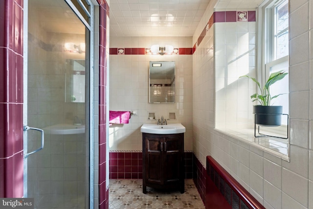 bathroom featuring vanity, radiator, tile patterned flooring, tile walls, and walk in shower