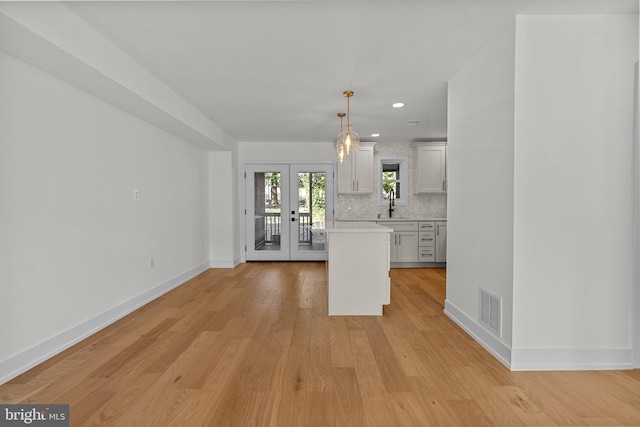 kitchen featuring french doors, light hardwood / wood-style flooring, decorative backsplash, decorative light fixtures, and white cabinetry